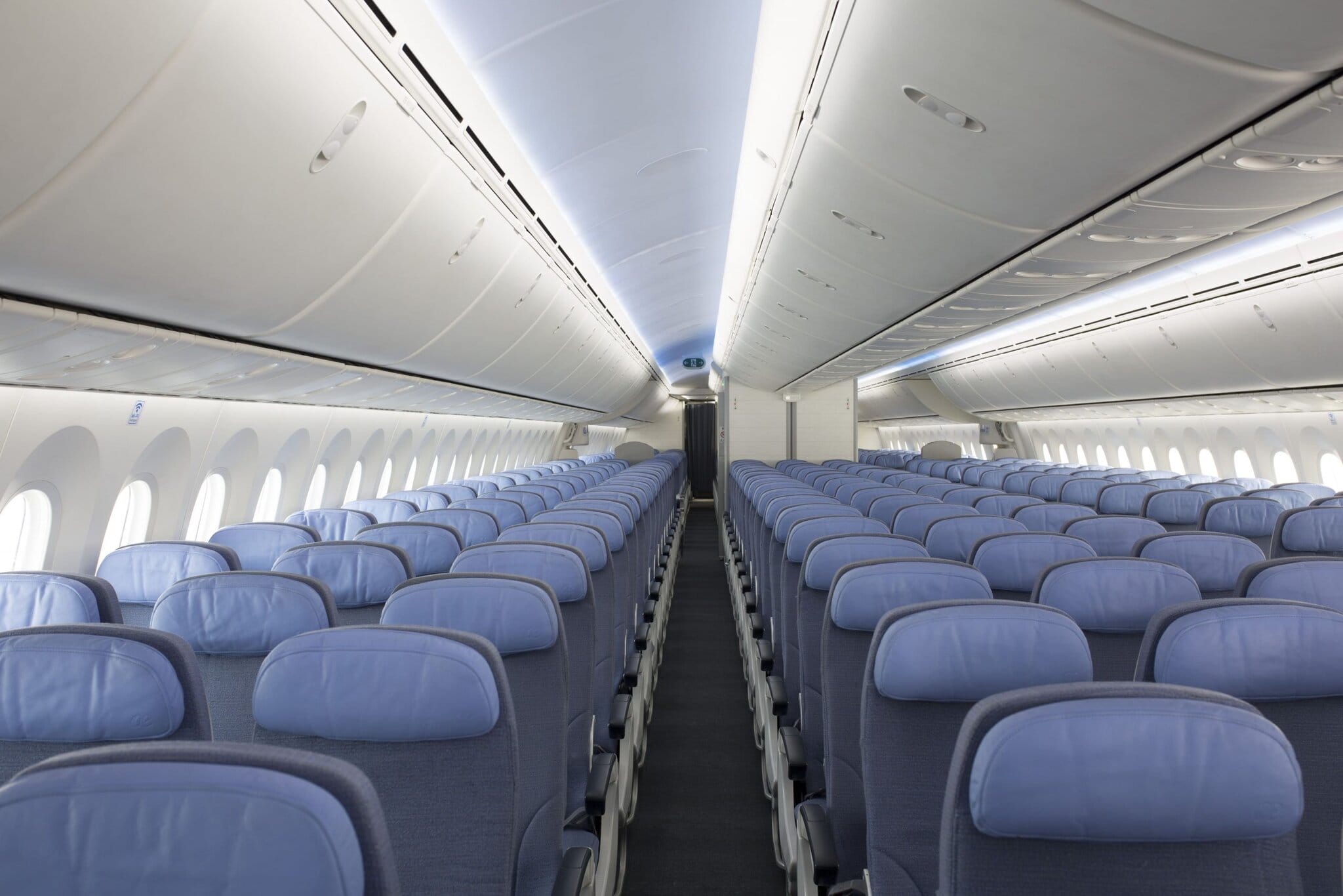 Spacious airplane interior with rows of blue seats and overhead storage, designed for comfortable travel.