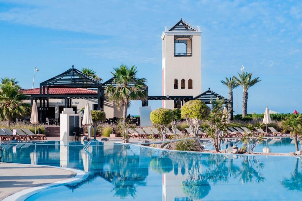 Luxurious hotel pool with palm trees and resort bar, sunny sky, tropical vacation atmosphere, Globalia Corp destination.